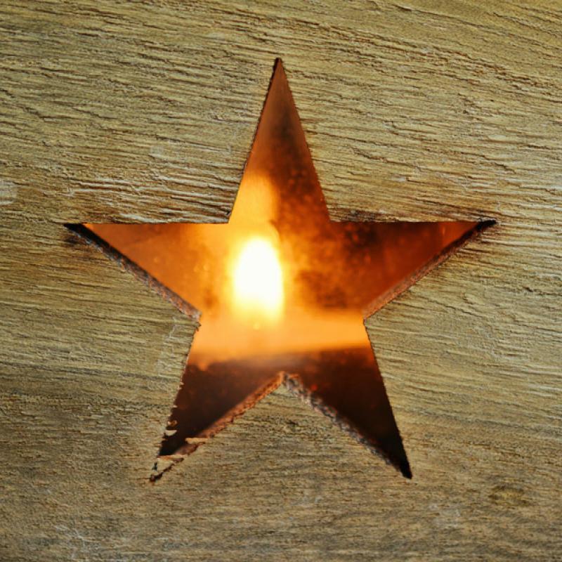 Holzbrett mit ausgeschnittenem Stern und dahinter eine Kerze