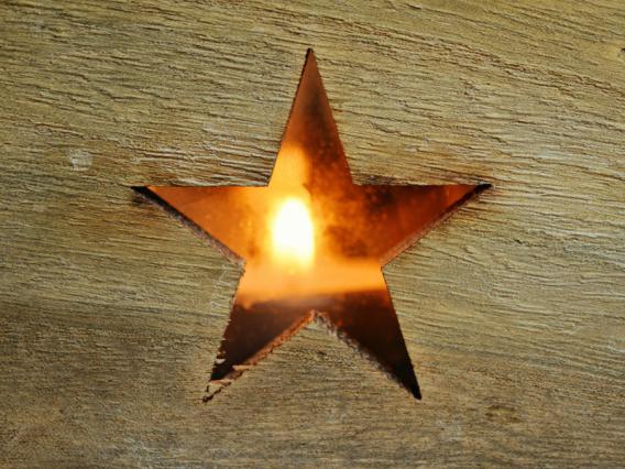 (c) pixabay Holzbrett mit ausgeschnittenem Stern und dahinter eine Kerze