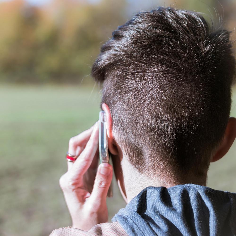 Ansicht von hinten: Eine Person telefoniert mit einem Mobiltelefon, das Gesicht ist nicht erkennbar.