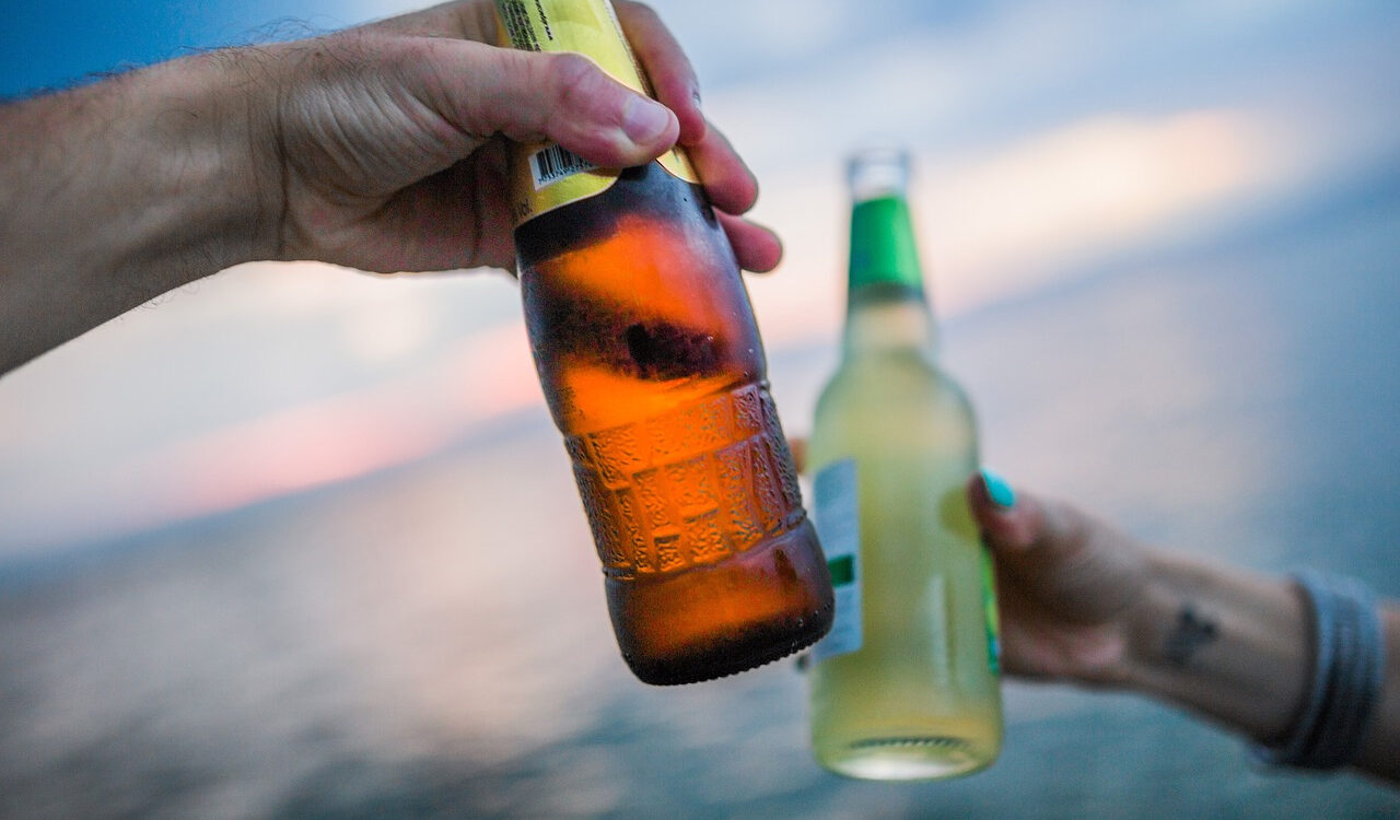 Zwei Hände die je eine Flasche mit Alkohol halten und sich zuprosten.