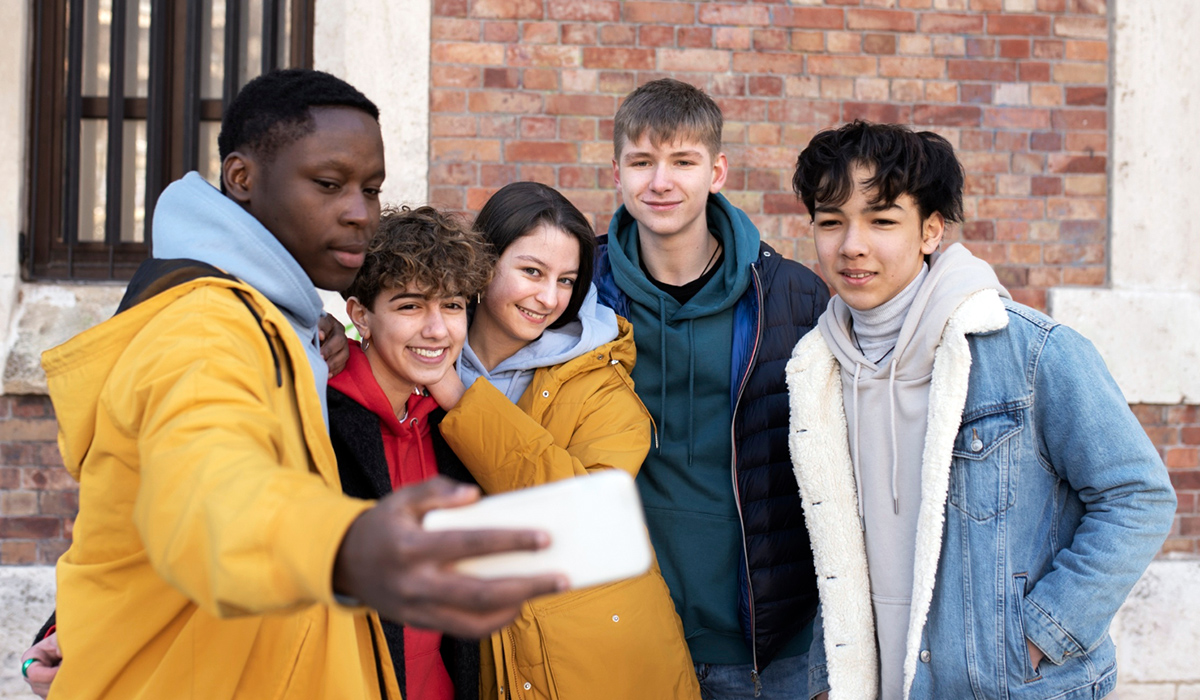 Jugendliche, Jungs und Mädels, unterschiedlicher Nationalität und Hautfarbe machen gemeinsam ein Selfie mit dem Handy.
