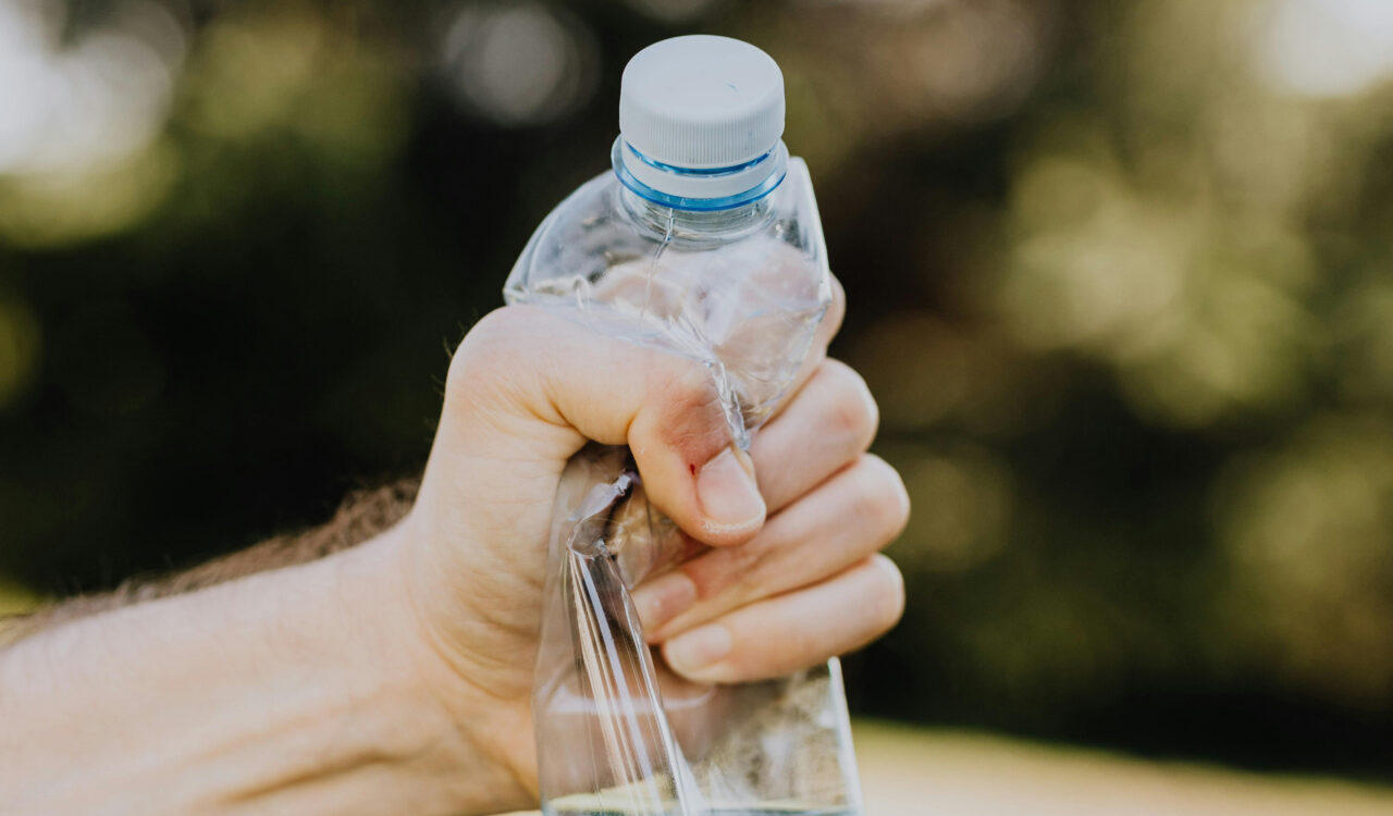 Eine Hand die eine Plastikflasche zerdrückt