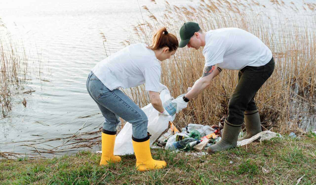 Jugendliche sammeln Müll ein, der an einem Gewässer liegt.