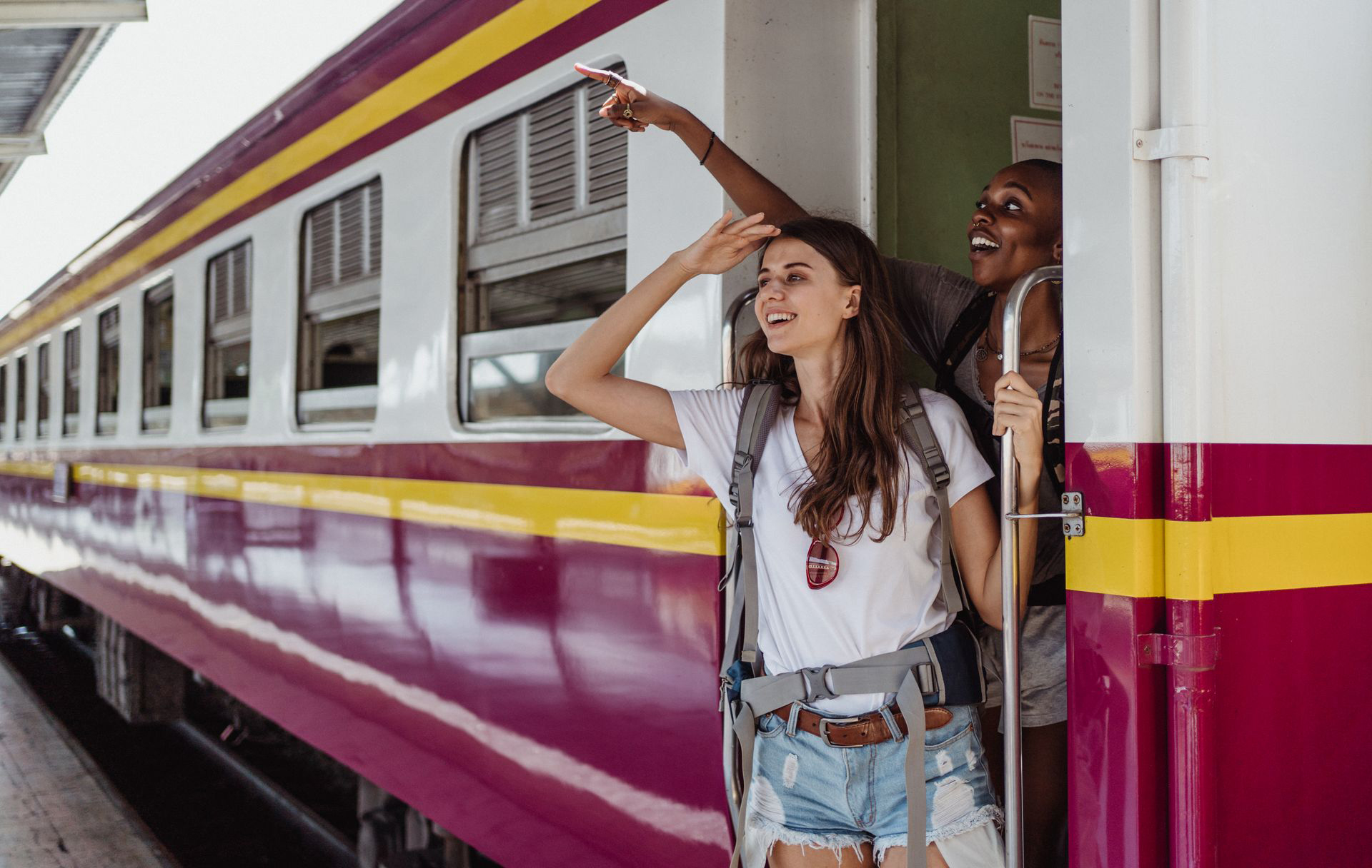 Zwei jugendliche Mädchen stehen an der Türe eines Zuges und schauen hinaus auf den Bahnsteig.