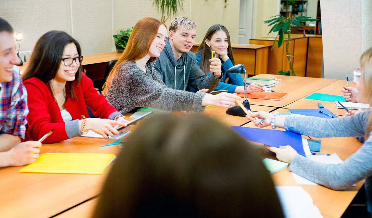 Mehrere junge Menschen sitzen an einem Tischen und entscheiden gemeinsam über wichtige Themen.