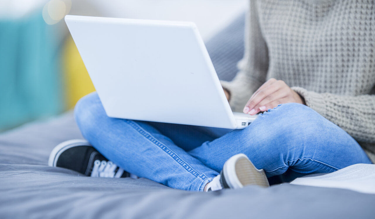 Eine jüngere Person im Teenageralter sitzt auf einer Couch und benutzt einen Laptop.