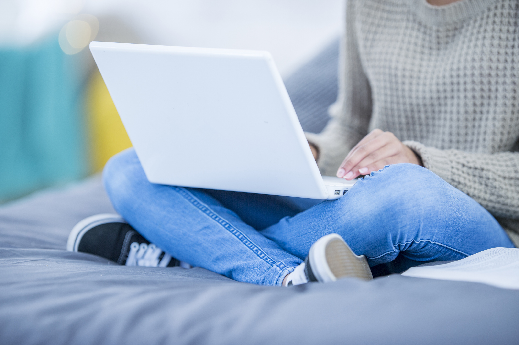 Eine jüngere Person im Teenageralter sitzt auf einer Couch und benutzt einen Laptop.