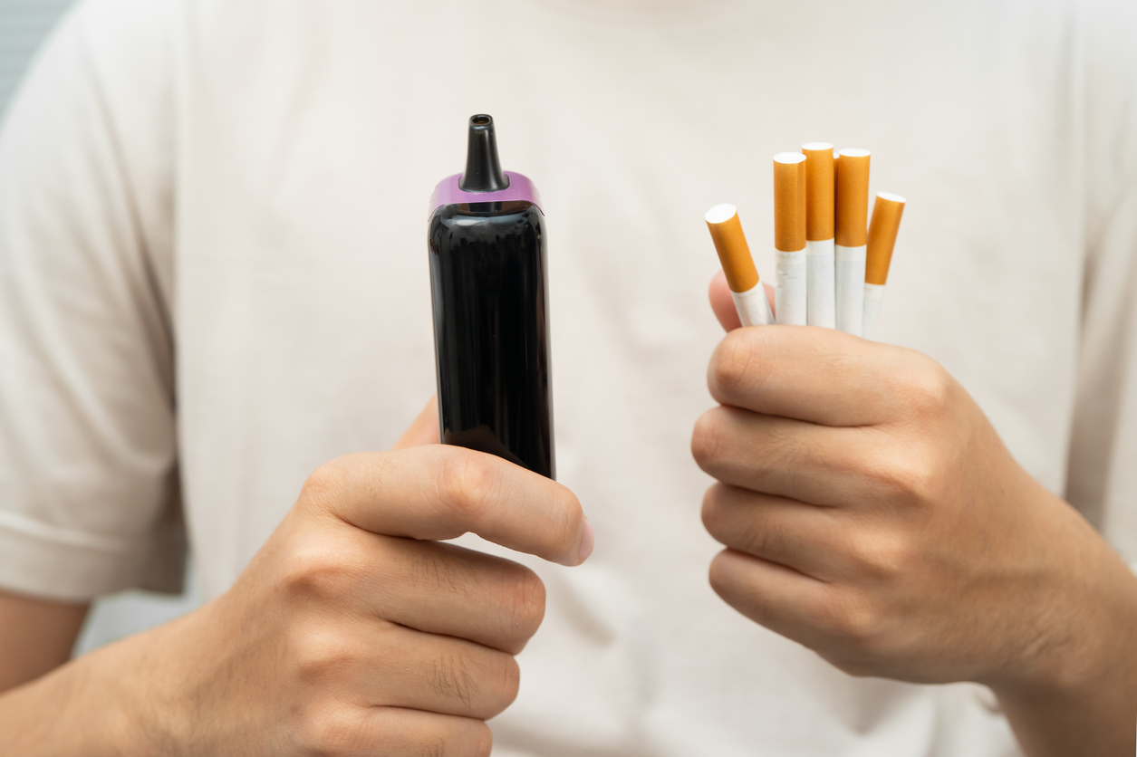Ein junger Mann hält in einer Hand mehrere Zigaretten, in der anderen Hand eine elektronische Zigarette oder Vape.